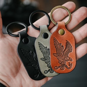 May include: Three leather keychains in black, gray, and brown, each with a metal ring. The keychains feature an embossed eagle design with the words "CARRY WHAT MATTERS". The brown keychain has a brass ring.