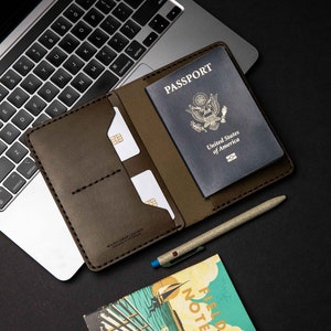 May include: A brown leather passport holder with a US passport inside, a pen, and a small notebook with the words "Field Notes" and "Acadia National Park Memo Book" on the cover.