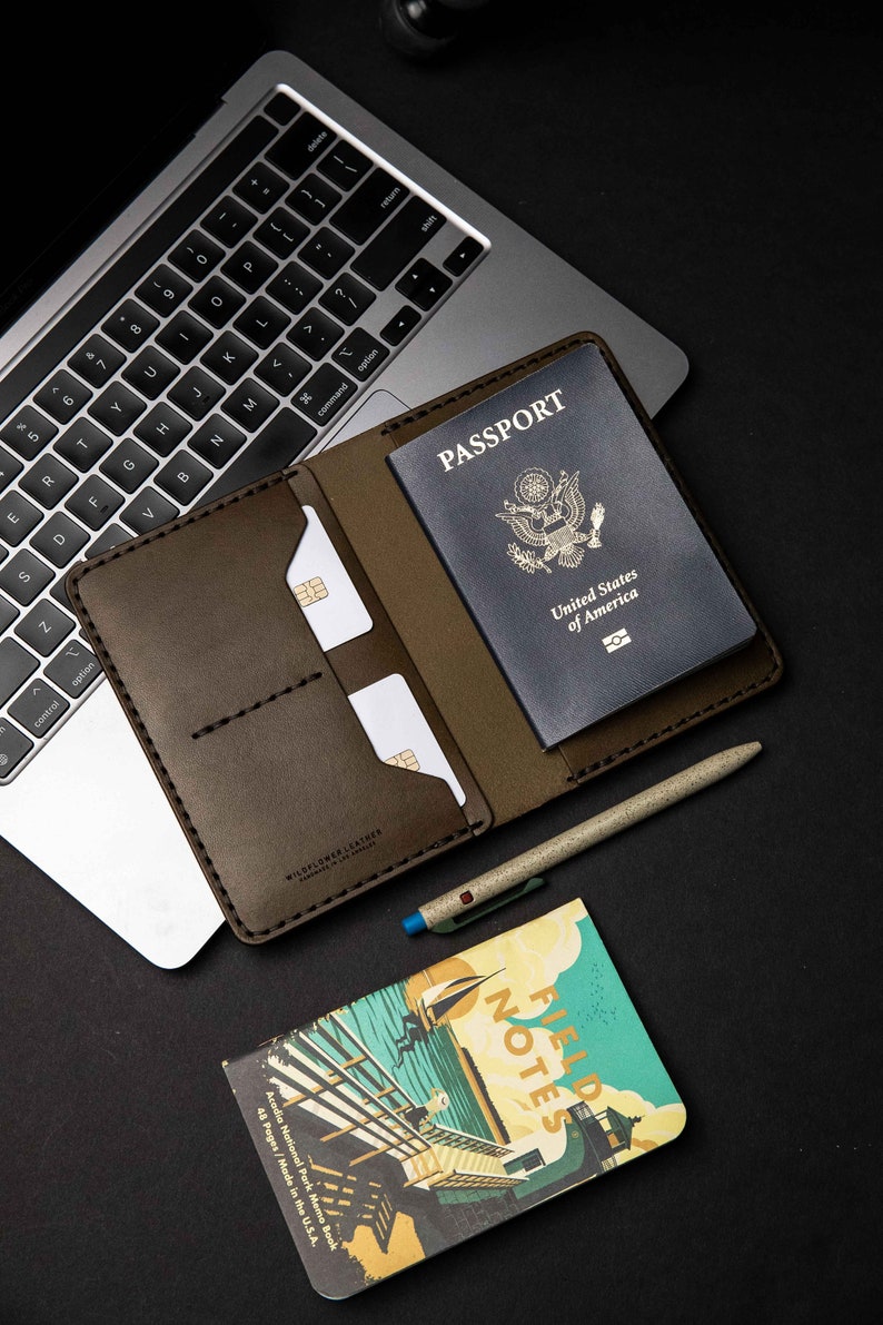 May include: A brown leather passport holder with a US passport inside, a pen, and a small notebook with the words "Field Notes" and "Acadia National Park Memo Book" on the cover.