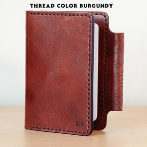 May include: A brown leather notebook cover with a topographic pattern and burgundy stitching. The cover has a pen loop and the initials "DJH" are embossed on the front.