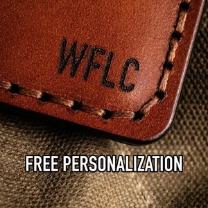 May include: Close-up of a brown leather wallet with the text "WFLC" embossed on the front. The wallet is lying on a brown canvas fabric. The text "FREE PERSONALIZATION" is visible below the wallet.