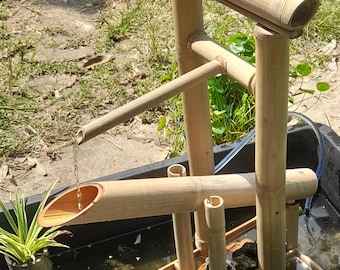 Può includere: Una fontana d'acqua in bambù con un piccolo stagno. La fontana è realizzata in bambù naturale e ha un aspetto rustico. L'acqua scorre dalla cima della fontana fino allo stagno.