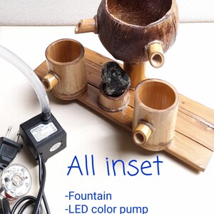 May include: A tabletop fountain made of bamboo and coconut with a black tourmaline stone. The fountain includes a small LED color pump and a clear plastic tube.