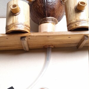 May include: A wooden fountain with a coconut shell as the center piece. The fountain has two bamboo cups on either side of the coconut shell. The fountain is connected to a black pump and a clear tube. The pump is connected to a clear round light with red LEDs.