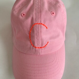 Puede incluir: Una gorra de béisbol rosa con una letra "C" bordada en naranja en la parte delantera.
