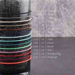 May include: A glass jar with 14 different colored cords wrapped around it. The cords are labeled with numbers and colors in German. The colors include black, gray, cream, tan, brown, dark blue, baby blue, turquoise, teal, mint, pink, red, burgundy, and orange.