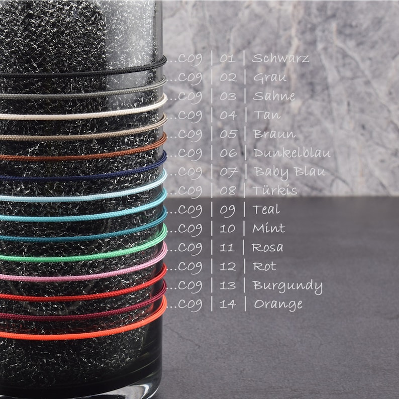 May include: A glass jar with 14 different colored cords wrapped around it. The cords are labeled with numbers and colors in German. The colors include black, gray, cream, tan, brown, dark blue, baby blue, turquoise, teal, mint, pink, red, burgundy, and orange.