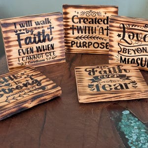 May include: A collection of five wooden plaques with inspirational quotes and phrases. The plaques are made of light brown wood with dark brown text. The phrases include "I will walk by Faith", "Created with a Purpose", and "Love Beyond Measure".