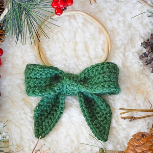 May include: A green crocheted bow with a wooden ring, surrounded by pine branches, pine cones, and red berries.