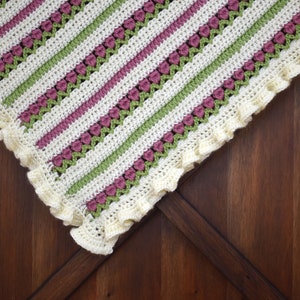 May include: A crocheted baby blanket with a white, green, and pink striped pattern. The blanket has a scalloped edge and is made with a delicate stitch.