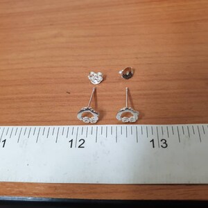 Op de afbeelding: Een paar zilveren oorbellen met een klein cirkelontwerp en heldere stenen. De oorbellen worden gemeten met een liniaal en zijn ongeveer 3 cm lang.