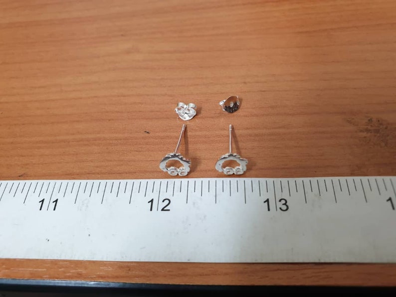 Op de afbeelding: Een paar zilveren oorbellen met een klein cirkelontwerp en heldere stenen. De oorbellen worden gemeten met een liniaal en zijn ongeveer 3 cm lang.