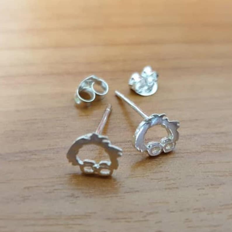 Op de afbeelding: Een paar zilveren oorbelletjes met een klein, gedetailleerd ontwerp. De oorbelletjes liggen op een houten oppervlak.