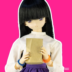 Könnte beinhalten: Eine Puppe mit schwarzen Haaren und lila Augen, die eine weiße Bluse und einen lila Rock trägt und eine braune Papiertüte hält. Die Puppe hat orangefarbene und blaue Armbänder. Der Hintergrund ist hellrosa.