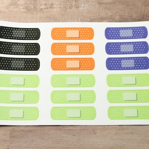 May include: A sheet of colorful adhesive bandages with different patterns. The bandages are in black, orange, green, and blue.