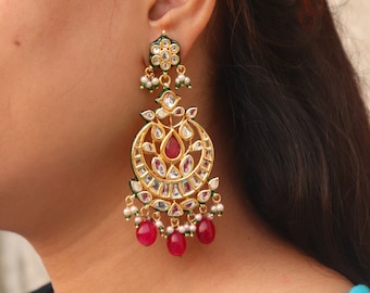 May include: Gold earrings with a large, ornate design featuring white and red stones. The earrings have a green enamel finish and dangle from a small pearl drop.