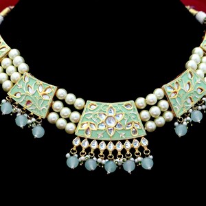 May include: A green and gold necklace with a floral design and pearl accents. The necklace has a central pendant with a larger floral design and a smaller floral design on each side.