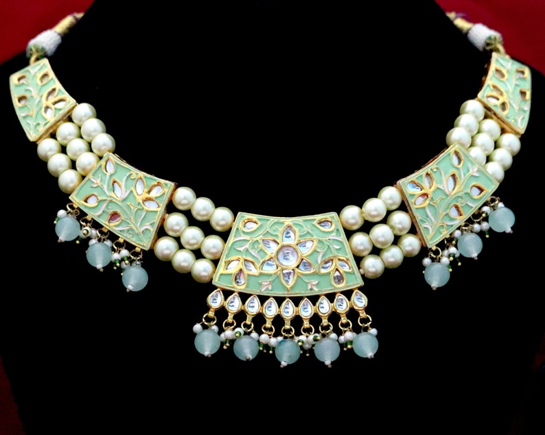 May include: A green and gold necklace with a floral design and pearl accents. The necklace has a central pendant with a larger floral design and a smaller floral design on each side.