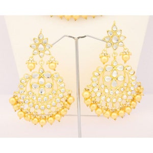 May include: A pair of gold earrings with pearl accents. The earrings feature a circular design with multiple layers of white stones.