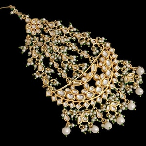 May include: Gold-toned headpiece with intricate floral and geometric designs, adorned with white pearl accents and green detailing. The headpiece features a crescent-shaped central element and dangling pearl strands, set against a black background.