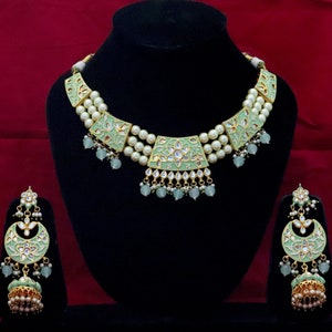 May include: A green and gold necklace set with pearl accents. The necklace features a multi-layered design with a central pendant. The earrings are dangle style with a similar design to the necklace.