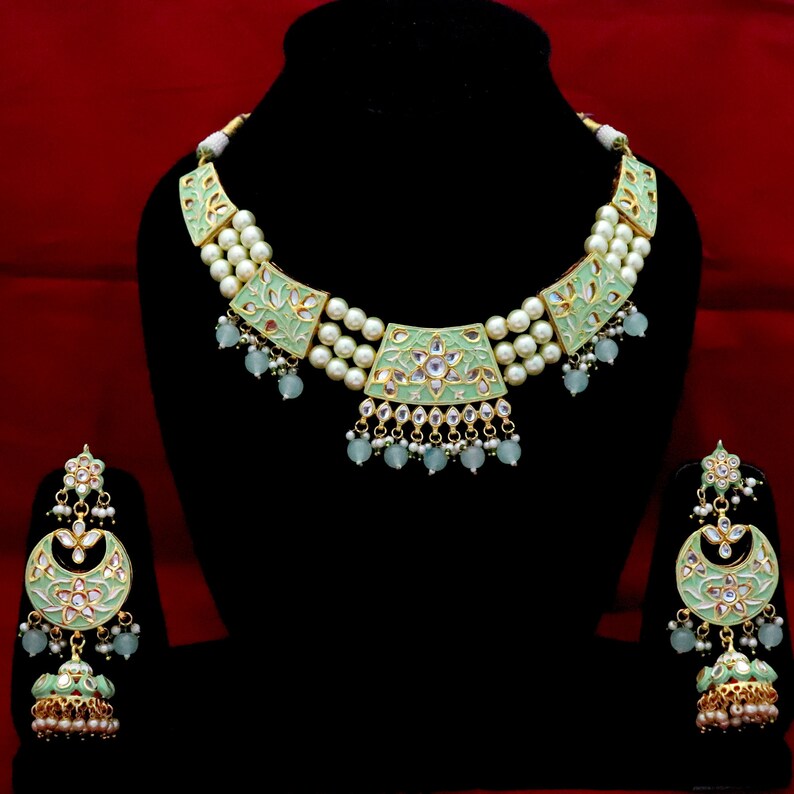 May include: A green and gold necklace and earrings set with pearl accents. The necklace has three rows of pearls and green enamel pendants with floral designs. The earrings are dangle style with a similar green enamel design.