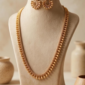May include: A gold-toned necklace and matching pair of earrings. The necklace features a long chain adorned with small, uniform, teardrop-shaped pendants. The earrings mirror this design, consisting of a circular arrangement of similar gold beads.