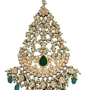 Puede incluir: Tocado dorado con una piedra verde esmeralda en forma de lágrima en el centro. El diseño presenta perlas blancas, piedras verdes más pequeñas y detalles dorados intrincados. Un accesorio delicado y elegante.