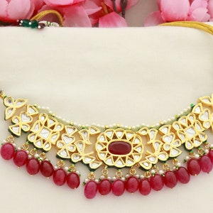 Könnte beinhalten: Eine goldene Halskette mit einem roten und weißen Steinmuster und roten Perlen. Die Halskette wird mit passenden Ohrringen geliefert.