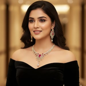 May include: A woman in a black off-the-shoulder dress, adorned with a diamond and ruby necklace and matching earrings. The gold jewellery features a central ruby stone and surrounding diamonds. The woman has dark hair and is smiling.