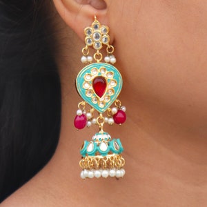 May include: Teal and gold dangle earrings with red and white accents. The earrings feature a teardrop-shaped design with a red stone in the center and a smaller teardrop-shaped design at the bottom.