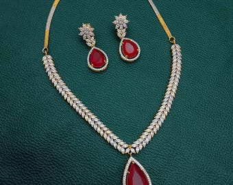 Puede incluir: Un collar de oro con un colgante en forma de lágrima engastado con piedras rojas y blancas. El collar se acompaña de pendientes a juego.