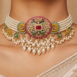 May include: A multi-strand pearl choker necklace featuring a central oval pendant with a red rectangular stone, surrounded by intricate gold-tone filigree, green and yellow enamel accents, and dangling white pearl drops along the lower edge.