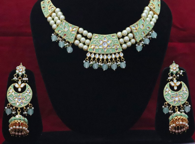 May include: A green and gold necklace and earrings set with pearl accents. The necklace has a layered design with three rows of pearls and a central pendant with a floral motif. The earrings are dangle style with a similar floral design.