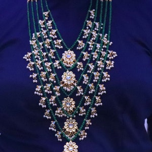 May include: A multi-layered necklace with green and white beads, gold accents, and intricate floral designs. The necklace features a cascading design with multiple strands of beads and decorative elements.