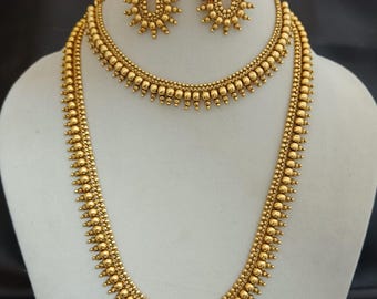 May include: A gold-colored jewelry set featuring a long necklace, a shorter necklace, and matching earrings. The necklaces and earrings are adorned with small, round beads and a sunburst design. The jewelry is displayed on a white mannequin.