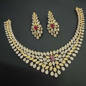 May include: A gold and silver necklace with a leaf design and red stones. The necklace is paired with matching earrings.
