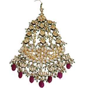 May include: An ornate gold-toned headpiece with a floral design. The headpiece features white, green, and red accents, with dangling ruby-colored beads. The intricate design includes small pearls and a hook for securing to the hair.
