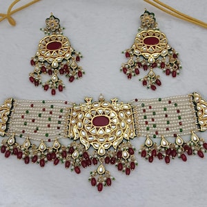 Könnte beinhalten: Ein verziertes Schmuckset mit einer Halskette und passenden Ohrringen. Das Set hat ein goldfarbenes Metall mit roten und weißen Akzenten. Die Halskette und die Ohrringe sind mit roten und weißen Perlen verziert.