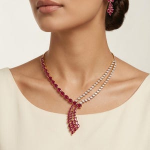 Puede incluir: Un collar de oro y un juego de pendientes a juego. El collar presenta un diseño de doble hebra con una fila de piedras preciosas rojas y una fila de piedras preciosas claras. Los pendientes tienen un diseño similar con piedras rojas.
