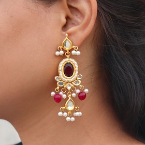 May include: Gold dangle earrings with a red gemstone, white pearls, and clear stones.
