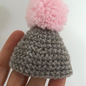 May include: A small gray knitted hat with a pink pom-pom on top.