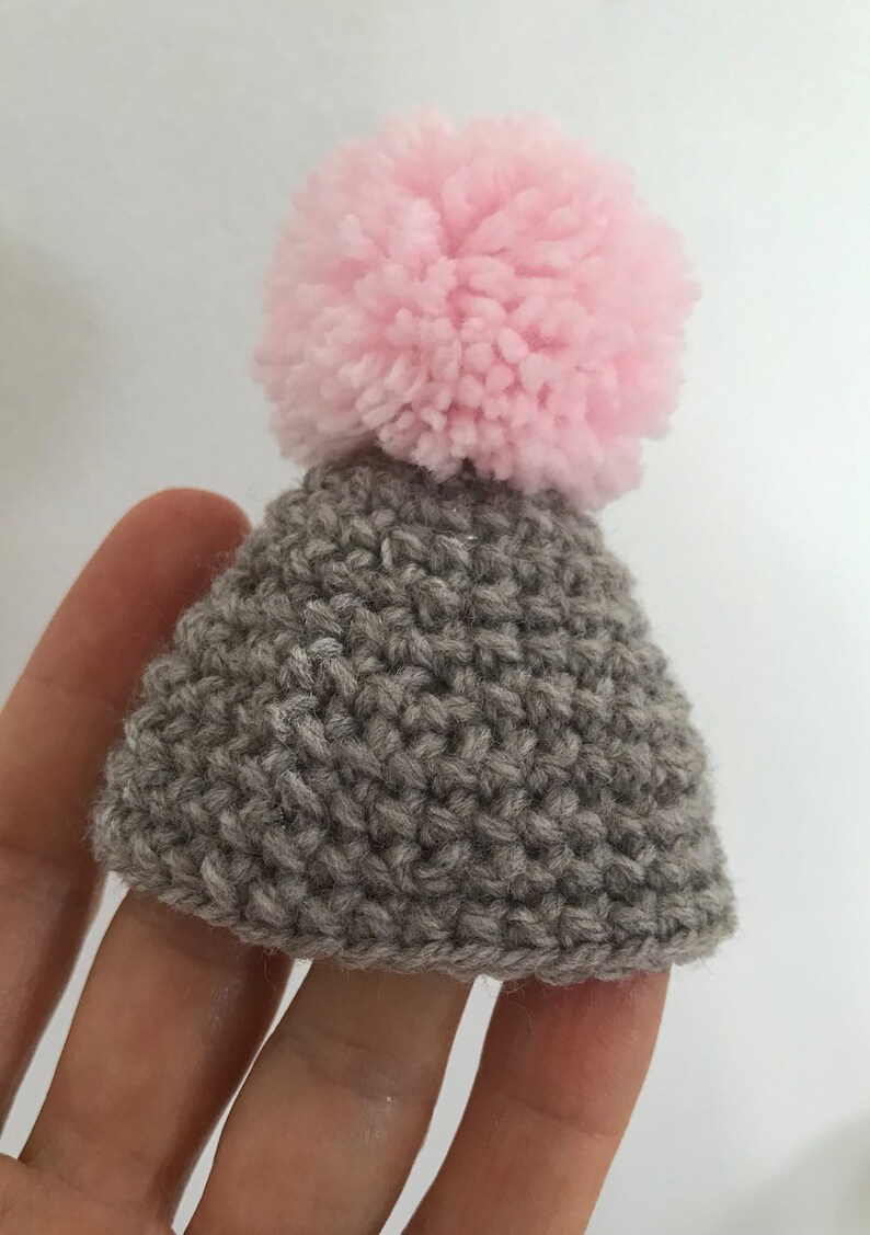 May include: A small gray knitted hat with a pink pom-pom on top.