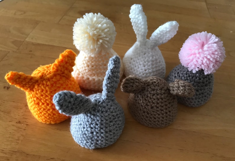 May include: Six crocheted hats in various colors and styles, including a white bunny hat, a pink pom-pom hat, and a gray hat with bunny ears.