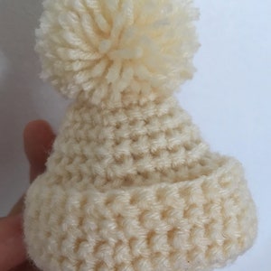 May include: A white crocheted beanie with a fluffy pom pom on top.