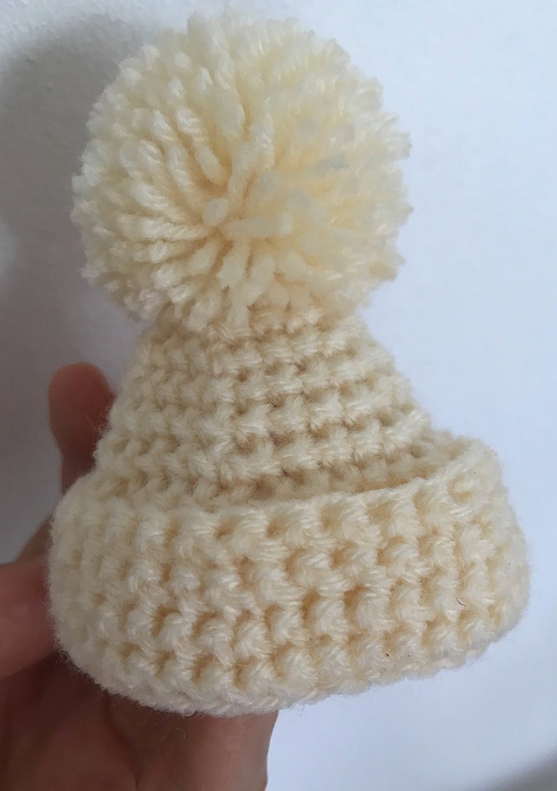 May include: A white crocheted beanie with a fluffy pom pom on top.