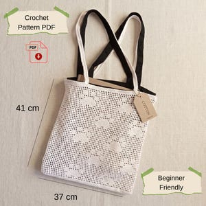 May include: White crochet tote bag with black handles, measuring 16 inches in height and 14.5 inches in width. The bag features a floral pattern and a cotton tag. Text on the image reads "Crochet Pattern PDF" and "Beginner Friendly".