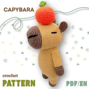 May include: Crochet pattern for a capybara amigurumi toy with an orange pumpkin on its head. The pattern is available in PDF format and is written in English. The pattern is called "CAPYBARA crochet PATTERN PDF/EN".