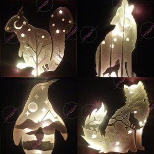 Puede incluir: Cuatro piezas de arte de pared de madera iluminadas que presentan una ardilla, un lobo, un pingüino y un zorro. Cada pieza tiene una silueta del animal con una escena de bosque detrás. Las escenas están iluminadas con luces LED blancas cálidas.
