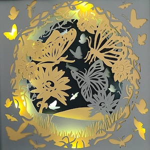 May include: A decorative wall art piece featuring a white background with intricate cut-out designs of butterflies and flowers in shades of gold and gray.